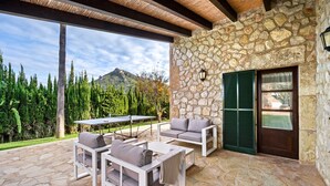 An outdoor patio with stone flooring, white furniture, and a stone wall. - Can Segue by Balearic Villas (Alcúdia)