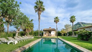 A swimming pool with lounge chairs, a small building with a tiled roof, and palm trees. - Can Segue by Balearic Villas (Alcúdia)