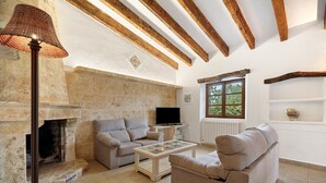 A cozy living room with a stone fireplace, a sofa, a coffee table, and a television. - Can Segue by Balearic Villas (Alcúdia)