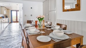 A dining area with a wooden table set for four, white plates, and a vase of flowers. - Longview Cottage - sleeps 6 guests  in 3 bedrooms (Wells-next-the-Sea)