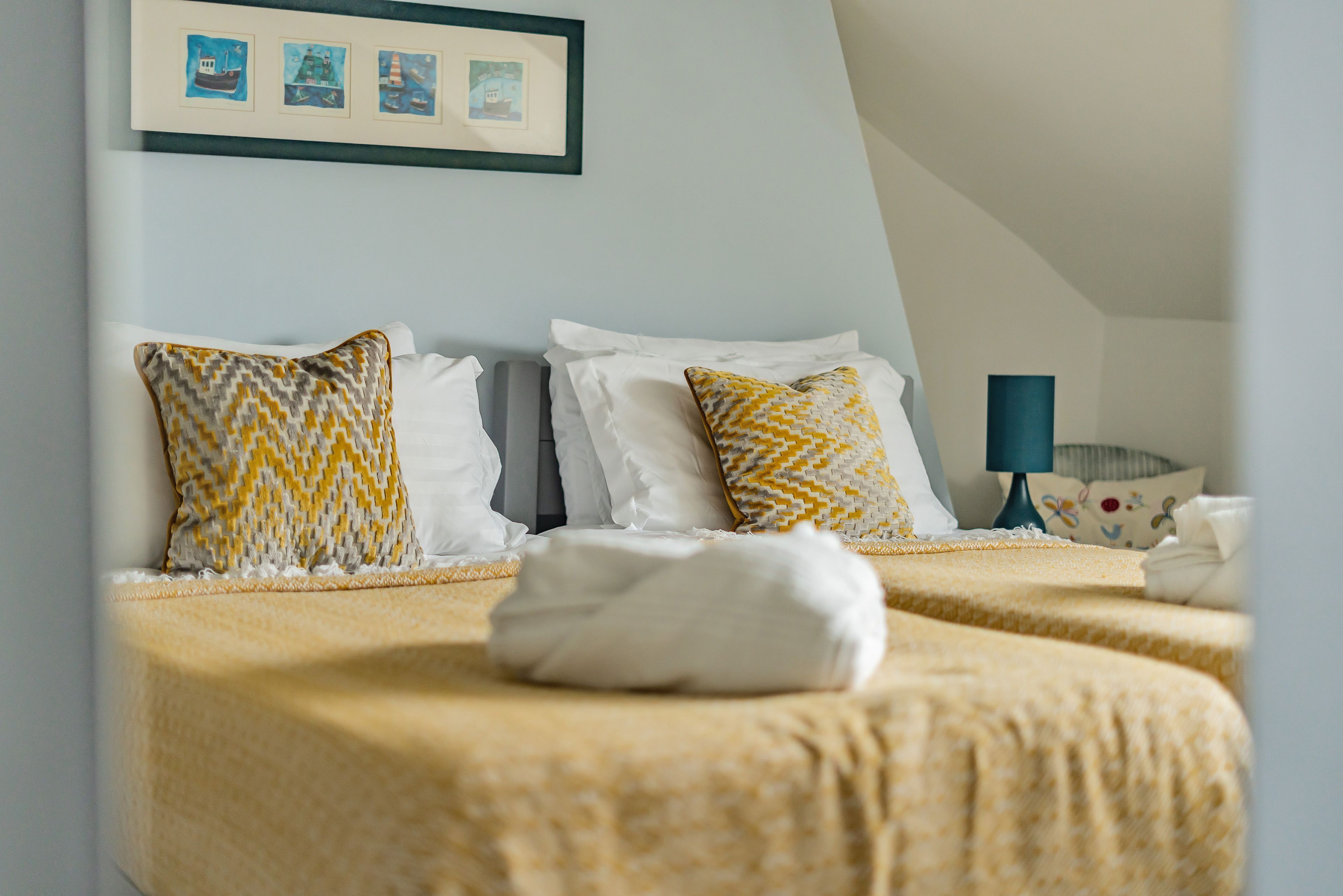 A hotel room with two beds, each with patterned pillows and a neatly folded white towel.