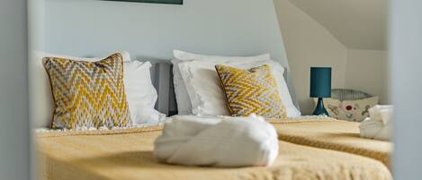 A hotel room with two beds, each with patterned pillows and a neatly folded white towel.