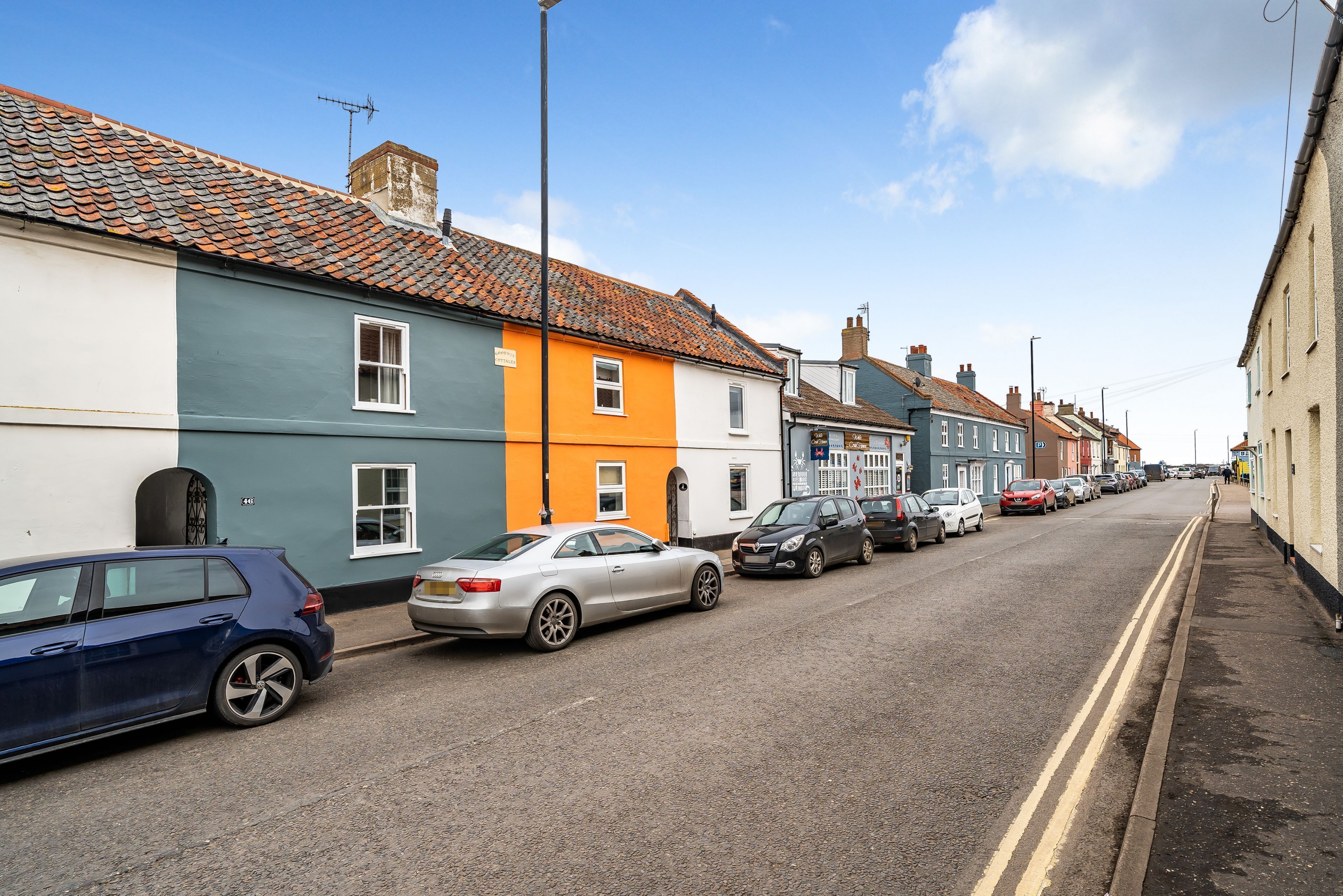 A street lined with colorful houses, parked cars, and a clear sky.
