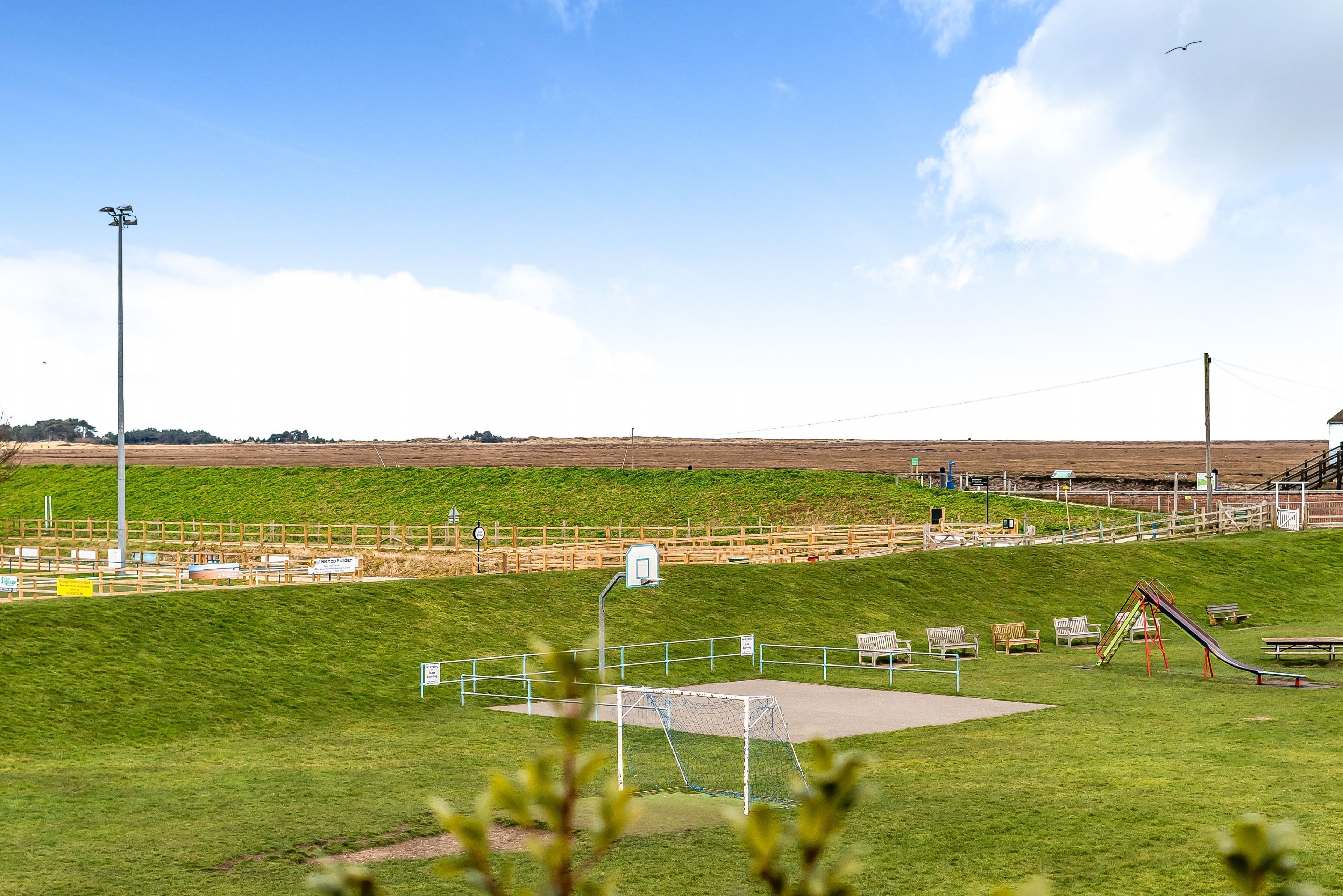 A park with a soccer field, playground, benches, and a clear sky.