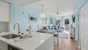 A modern kitchen with a marble countertop, a sink, and a dining area with a table and chairs. - Sunset Vistas 403s (Treasure Island)