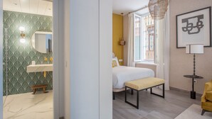 Ein modernes Hotelzimmer mit Bad, einem Bett, einer Bank und einem gelben Sessel.