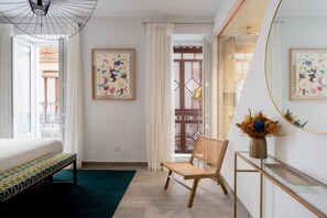 A hotel room with a bed, a bench, a chair, a mirror, and artwork on the walls. - Hernando Colón Olehousing 2 (Sevilla)