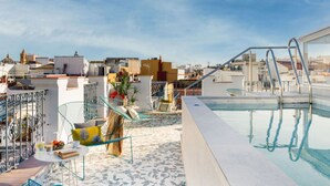 Ein Poolbereich auf dem Dach mit freiem Blick auf die Stadtlandschaft, eine Sitzgelegenheit mit Tisch und Stühlen sowie eine Treppe zum Pool.