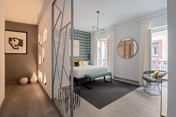 Quarto moderno com cama, espelho redondo, um banquinho e vista para o exterior.
