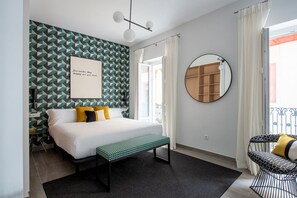 Quarto com uma cama, um banquinho, um espelho redondo e uma parede com padrão geométrico.