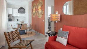 Un salon moderne avec un canapé rouge, des fauteuils à motifs et un coin repas, la cuisine étant visible au fond.