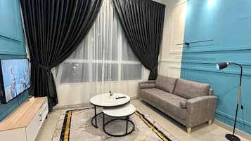 A living room with a sofa, a small round table, a TV, and a window with curtains.