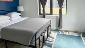 Une chambre d’hôtel avec un lit, une fenêtre avec des rideaux, une lampe et un tableau au mur.