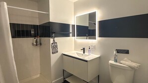 Une salle de bain moderne avec un lavabo blanc, des toilettes et une douche. Un panneau est affiché sur le mur avec la mention suivante : « Veuillez ne jeter dans les toilettes que du papier hygiénique. »