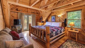Camera da letto in baita di legno con un letto di legno, un divano, una televisione e una finestra con persiane.