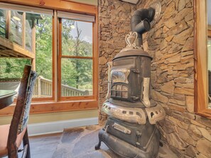 A wood-burning stove in a stone-walled room with large windows overlooking a wooden deck. - River's Edge Retreat (Sevierville)