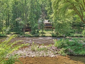 A cabin surrounded by dense forest and a flowing river. - River's Edge Retreat (Sevierville)