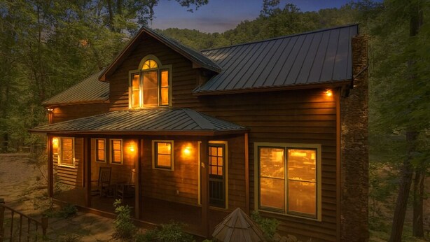 A wooden cabin with a porch and multiple windows, surrounded by trees. - River's Edge Retreat (Sevierville)