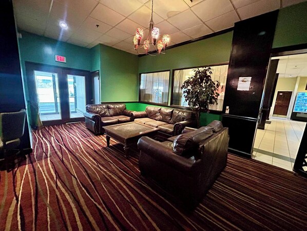 A lobby with a brown leather sofa set, a patterned carpet, and a chandelier.