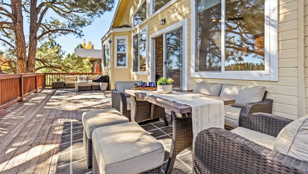 A covered outdoor patio with wicker furniture, a wooden table, and a stone fireplace. - NEW Cabin | Pool Table | Golf Course | AC | EV Charger (Flagstaff)