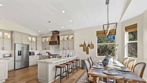 A modern kitchen with a central island, bar stools, and a dining area with a wooden table and chairs. - NEW Cabin | Pool Table | Golf Course | AC | EV Charger (Flagstaff)