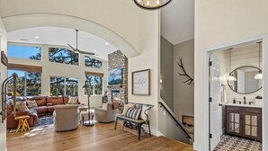 A spacious living room with a fireplace, a stone accent wall, and a large window overlooking trees. - NEW Cabin | Pool Table | Golf Course | AC | EV Charger (Flagstaff)