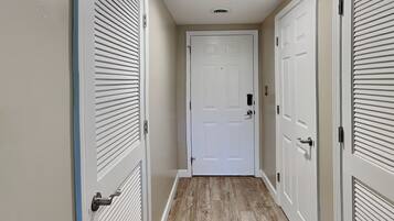 Un pasillo con piso de madera, puertas blancas con persianas en la parte superior y una puerta blanca al final.