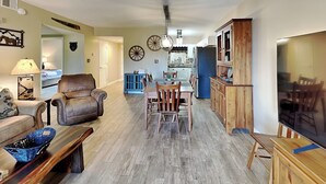 Een ruime woonkamer met een bruine leren bank, een houten eettafel met stoelen, en een keuken met houten kastjes en een koelkast.