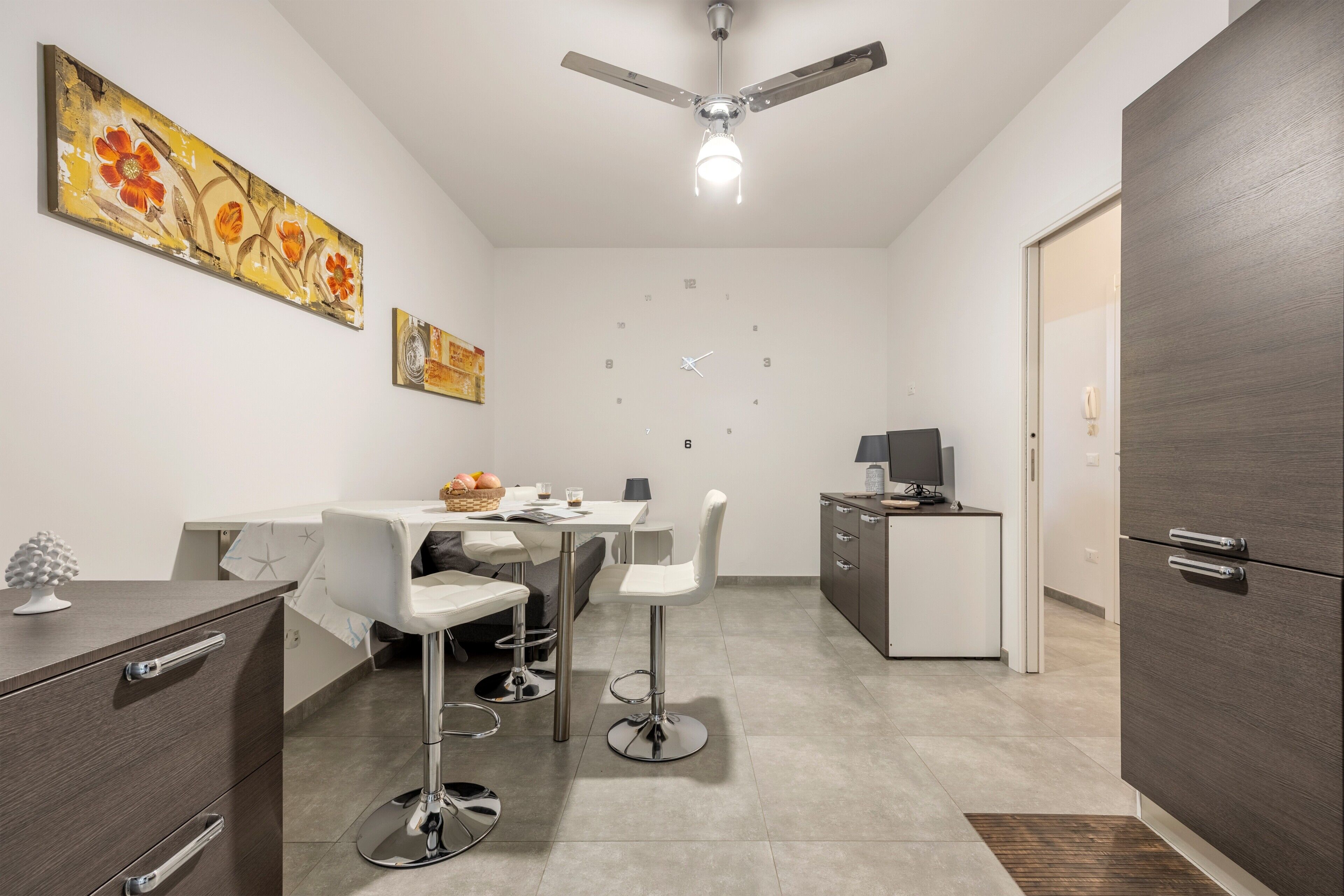 Una cocina moderna con comedor, ventilador de techo y un reloj en la pared.