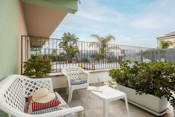 A balcony with white furniture, a table with a glass of wine, and a view of the sea. - Holiday Home 'Calarossa Tourist House Di Ale & Anny' with Sea View, Wi-Fi and Air Conditioning (terrasini)