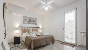 A bedroom with a bed, bedside table, wall-mounted air conditioner, ceiling fan, and a large window with frosted glass. - Holiday Home 'Calarossa Tourist House Di Ale & Anny' with Sea View, Wi-Fi, and Air Conditioning (terrasini)