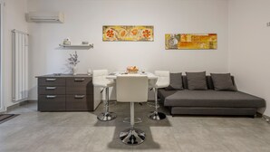 A modern living room with a sofa, a dining table with chairs, a cabinet, and two wall-mounted artworks. - Holiday Home 'Calarossa Tourist House Di Ale & Anny' with Sea View, Wi-Fi, and Air Conditioning (terrasini)