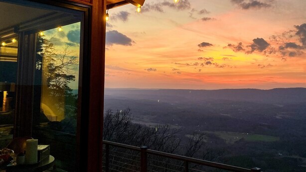 Ein Holzgebäude mit Glaswand, Feuerstelle und Blick auf die Landschaft.