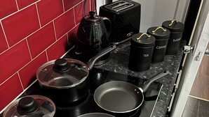 Cuina amb recipients de cuina negres, com ara casseroles i paelles, i tasses negres sobre el taulell.