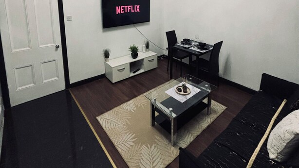 Un saló modern amb televisió de pantalla plana, una taula de menjador, un sofà i un rellotge decoratiu a la paret.