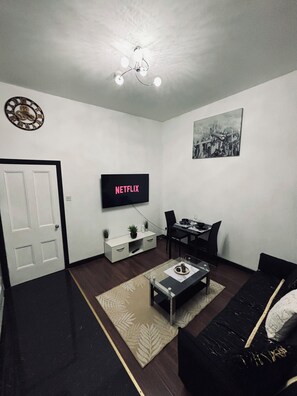 Een moderne woonkamer met een flatscreen televisie, een eettafel, een bank en een decoratieve klok aan de muur.