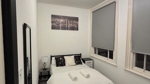 Un dormitori ben organitzat amb un llit, una taula de nit, una làmpada i un quadre de paisatge urbà a la paret.