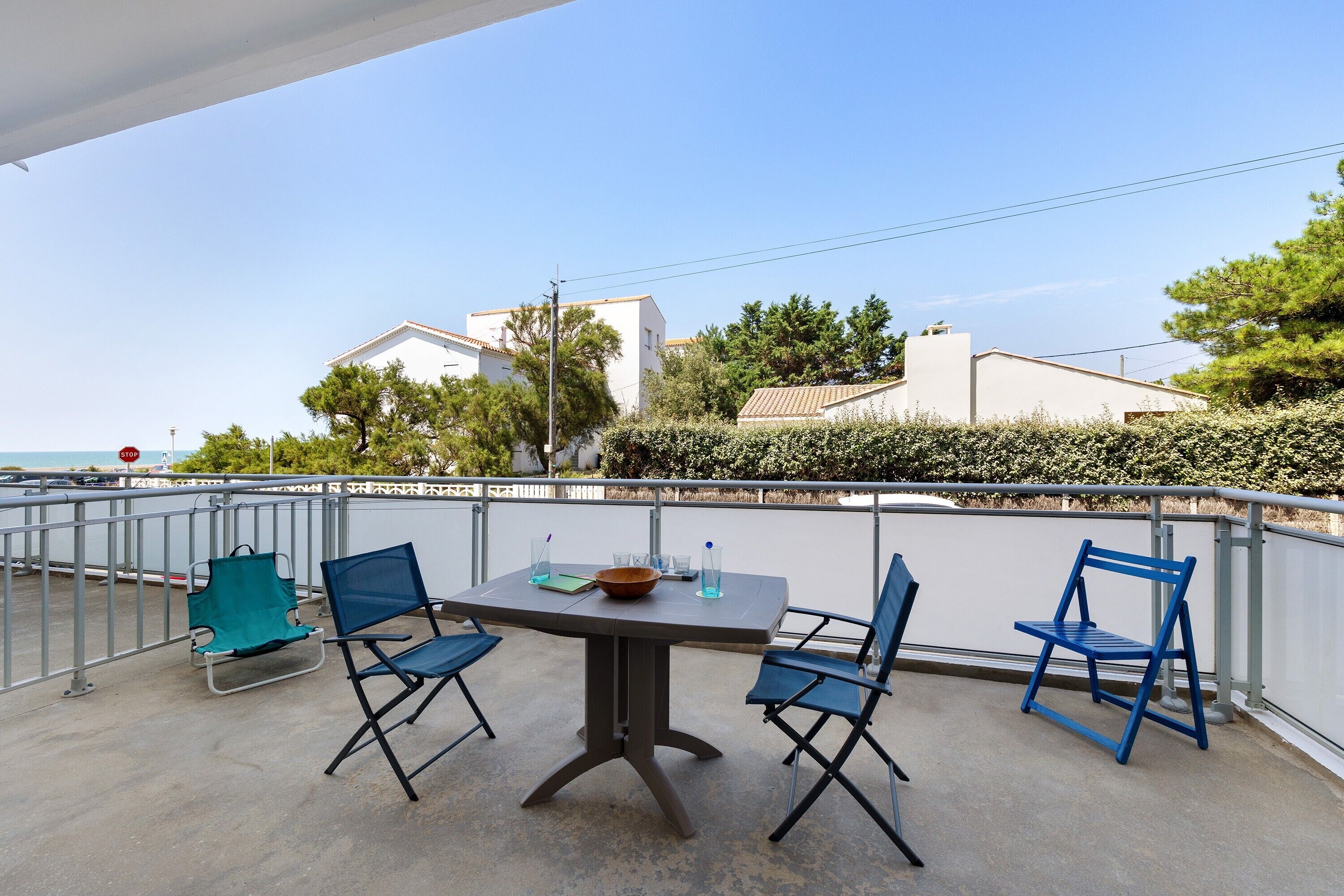 A balcony with a table and chairs, a view of the sea, and buildings in the background.