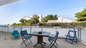 A balcony with a table and chairs, a view of the sea, and buildings in the background.