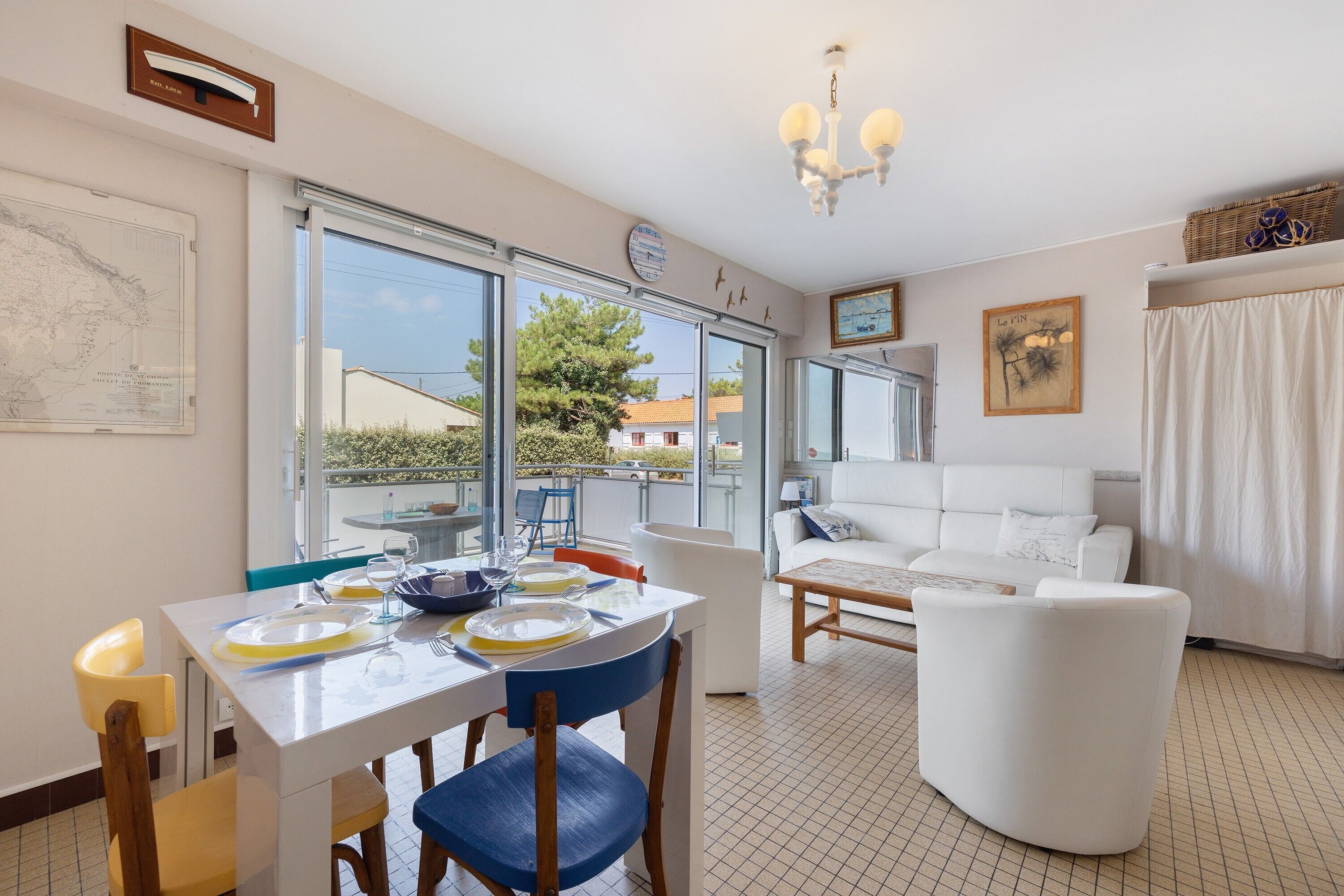 Un coin repas avec une table dressée pour deux personnes, un canapé blanc et une grande fenêtre donnant sur l’extérieur.