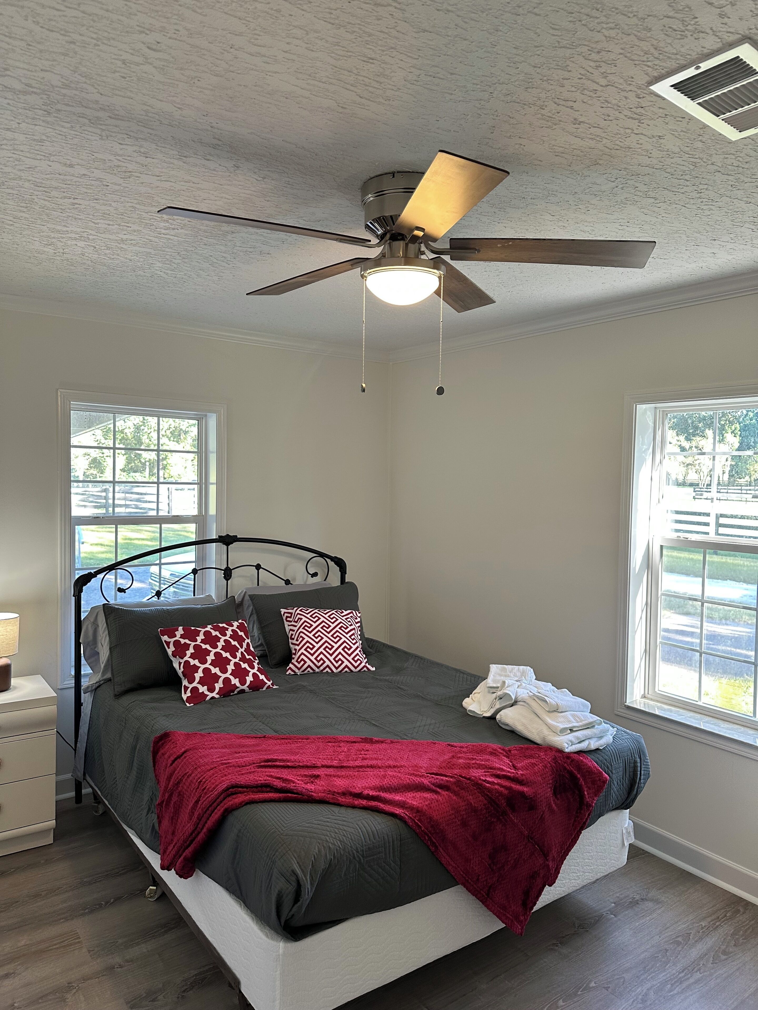 Una camera da letto con un letto, un ventilatore a soffitto e due finestre.