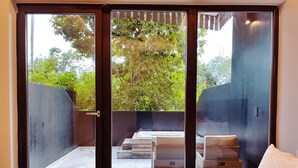 Un dormitorio con un amplio ventanal corredera que da a un espacio exterior con jacuzzi y mobiliario de mimbre.