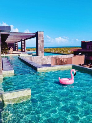 Una piscina de blau clar amb un flotsam de flamenc rosa, envoltada per un pont de fusta i una construcció de pedra.