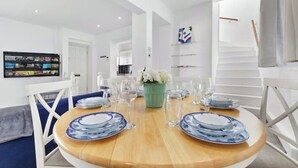 A dining area with a round wooden table set for four, surrounded by white chairs. A green vase with white flowers is placed in the center. - Modern Spacious 2 Bedroom House in Central London (Kensington )