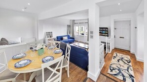 A spacious living area with a dining table set for four, a blue sofa, and a staircase leading to another level. - Modern Spacious 2 Bedroom House in Central London (Kensington )