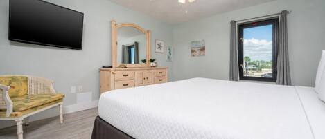 A bedroom with a bed, a chair, a dresser, a mirror, a ceiling fan, and a window with a view.