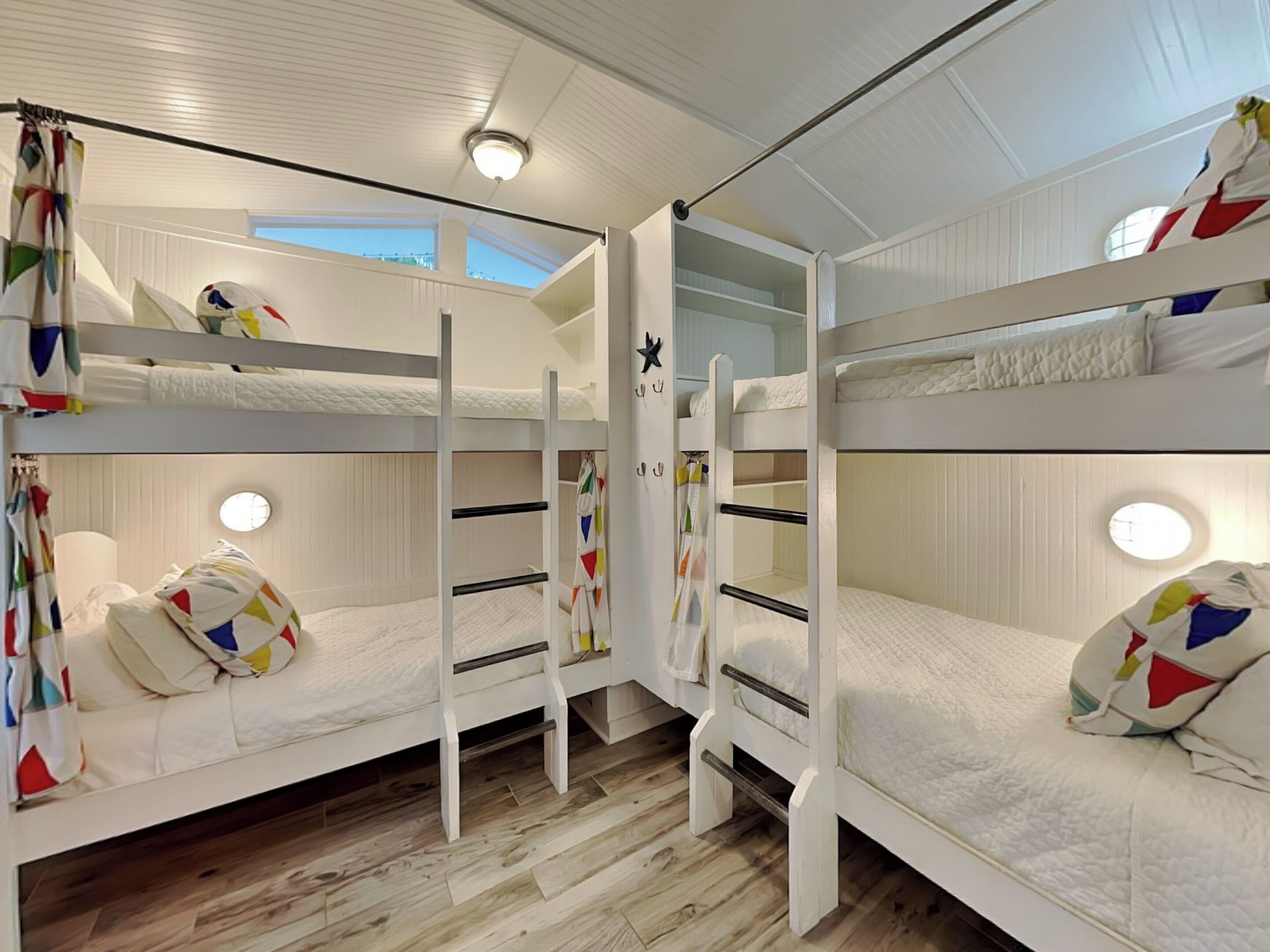 Une chambre avec des lits superposés, aux murs blancs, dotée d’un plancher en bois et d’une fenêtre laissant entrer la lumière naturelle.