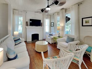 A living room with a fireplace, white furniture, wicker chairs, and a television. - Coast A While (Tybee Island)