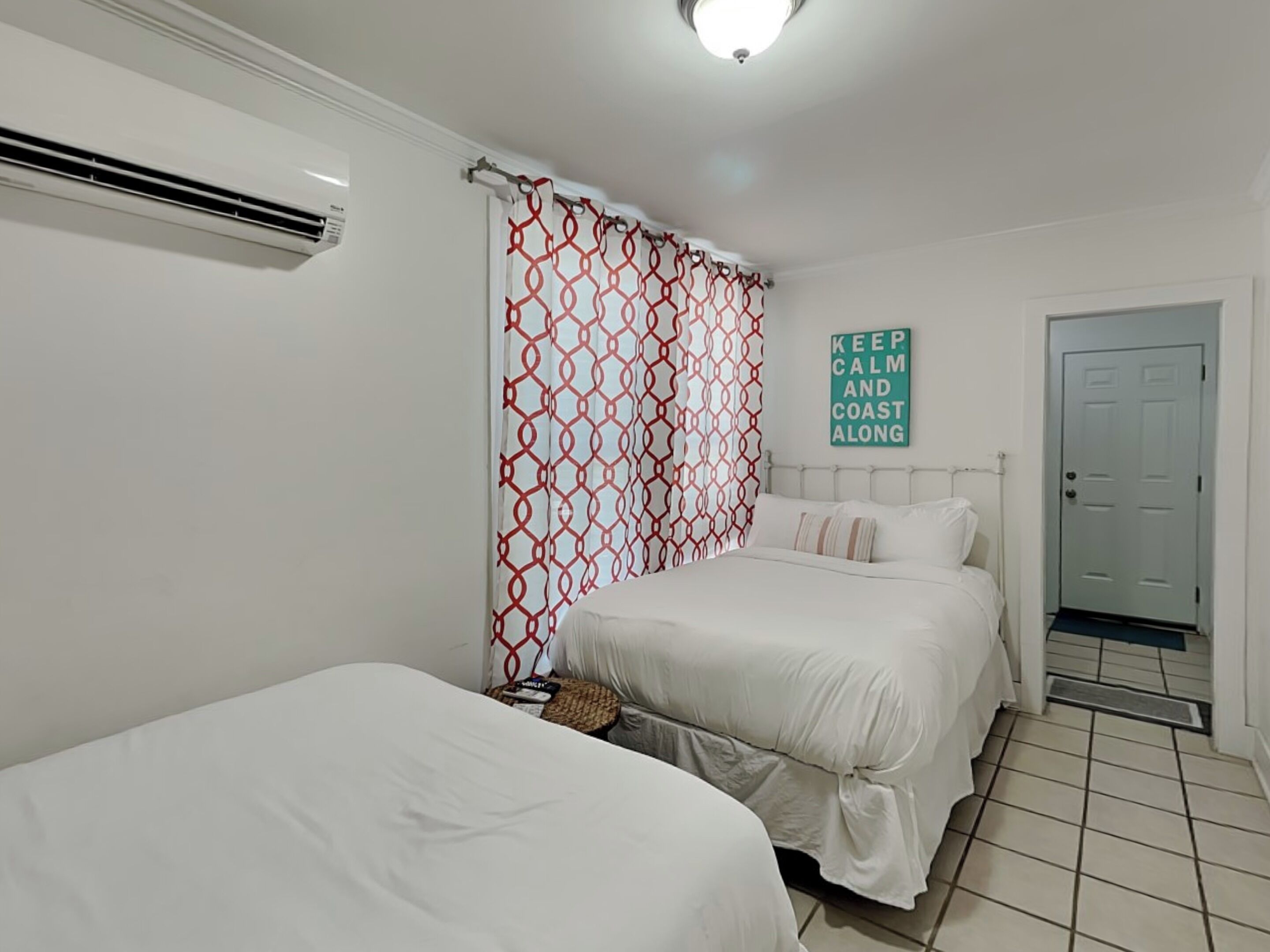 Un dormitorio con dos camas, una cortina estampada, un letrero motivacional y una puerta.