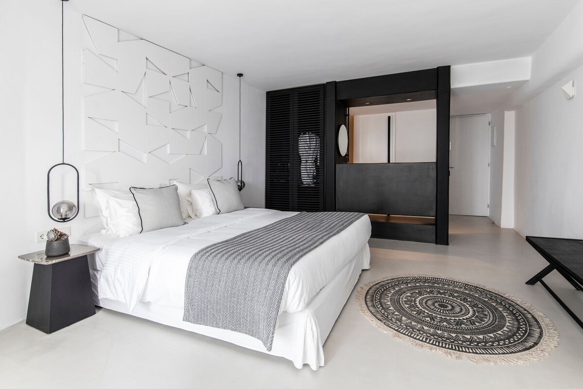Een moderne slaapkamer met een groot bed, een decoratieve wand, een zwarte bank en een kamerkleed met een patroon.